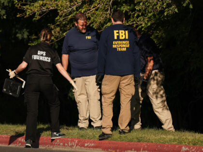 Law enforcement officials, including members of the FBI, investigate a wooded area near th