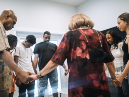 A large multi-generational group of family relatives holds hands and prays together in a l
