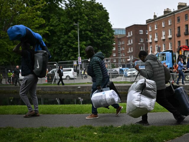 People carry their belongings as they leave from a makeshift camp set up by migrants, as t