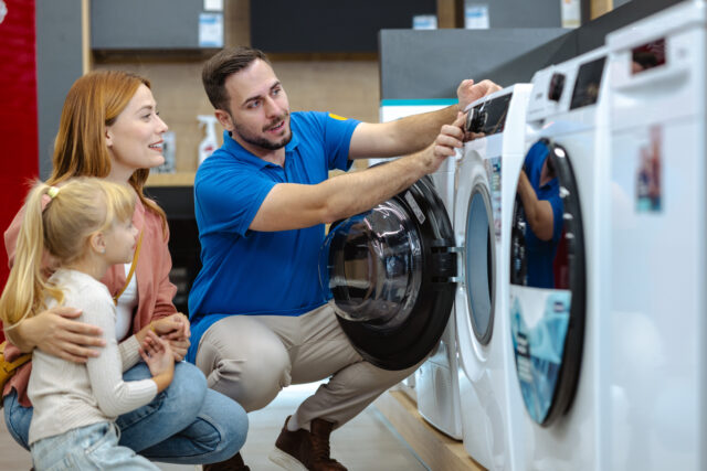 Mother and her daughter choosing new washing machines at an appliance store A friendly salesman shows a family the features of a washing machine in an appliance store