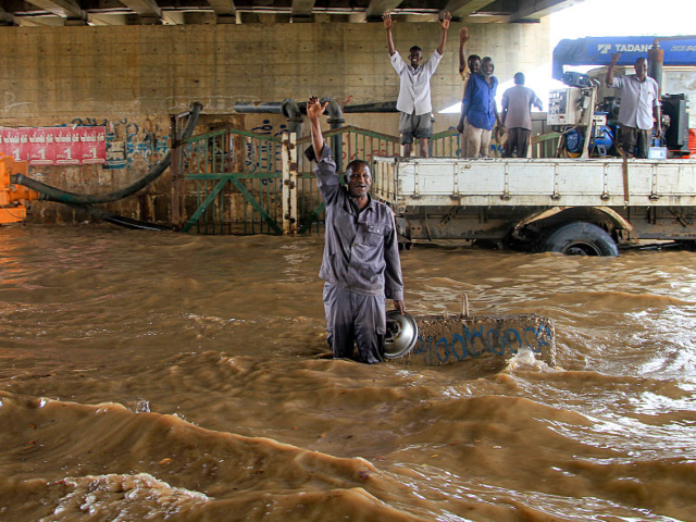 GettyImages-2231659094 TOPSHOT - Municipal workers react while operating a pump draining a flooded highway overpa