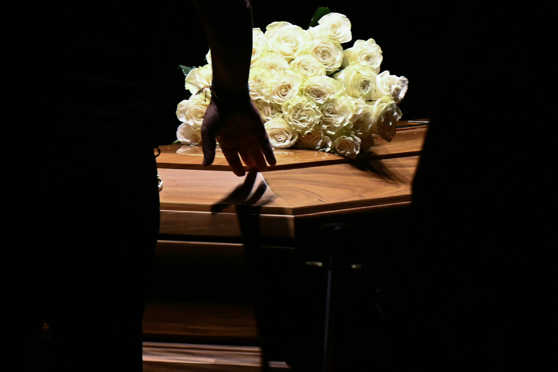 A man touches the coffin of late Italian fashion designer Giorgio Armani lying-in state for two days at the Armani Theatre in Milan as a picture of him is seen on a screen, on September 6, 2025. Giorgio Armani died on September 4, 2025 at 91. (Photo by Stefano RELLANDINI / AFP) (Photo by STEFANO RELLANDINI/AFP via Getty Images)