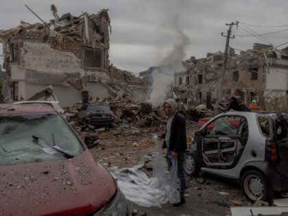 A man prepares to cover a damaged car with a plastic sheet at the site of heavily damaged