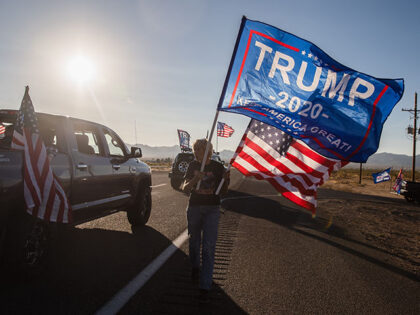 A woman waves a Trump and a US National flag as a caravan of cars from Kingman drives past