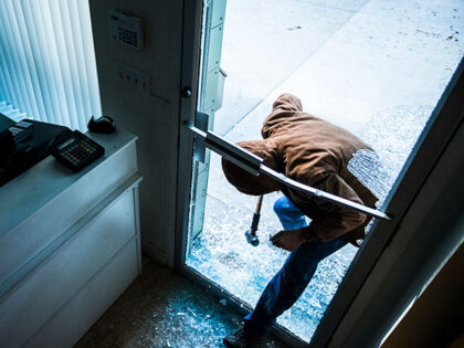 A robber using a sledgehammer to break the glass of a retail store.