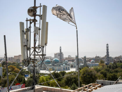 A Taliban flag flutters near telecom equipment installed over a rooftop providing internet