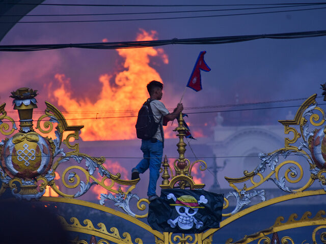 nepal-gen-z-protests-sept9-2025-getty KATHMANDU, NEPAL-SEPTEMBER 9: A man is hanging a pirate flag as smoke and flames rise from