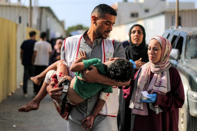 A worker at al-Awda Hospital carries a child who was injured by reported Israeli bombardme