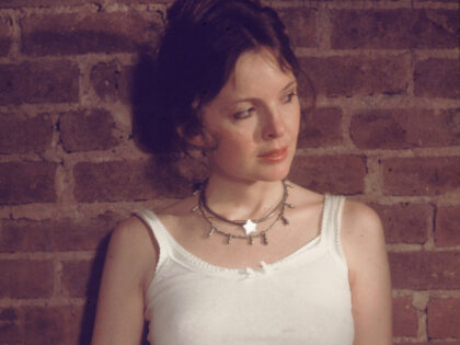 American actor Diane Keaton wears a white tank top and leans against a brick wall in a sce