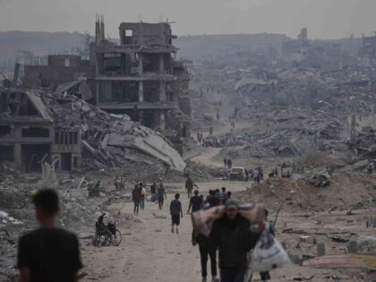 Displaced Palestinians walk with their belongings along the heavily damaged Al-Jalaa Stree