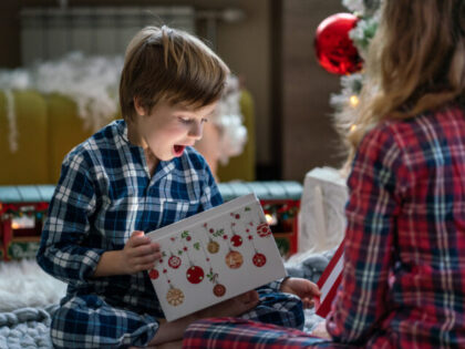 Surprised little boy opening Christmas present whit her sister at home