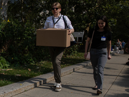 Recently laid off U.S. State Department employees carry boxes as they walk out of the Harr