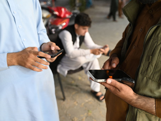 TOPSHOT - Afghan men use their mobile phones in Kabul on October 1, 2025. Mobile networks