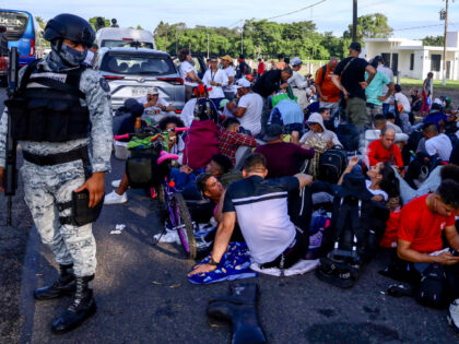 A member of the Mexican National Guard stands guard over migrants who are part of a carava