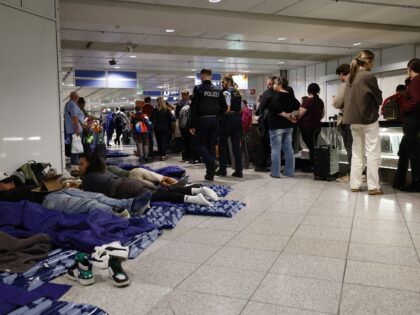 Passengers sleep on inflatable mattresses on the ground while others queue up next to them