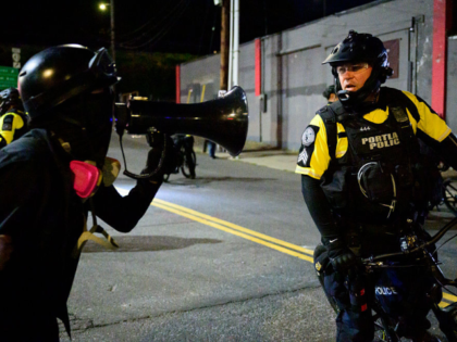 A protestor shouts in a megaphone toward a Portland Police officer near an Immigration and