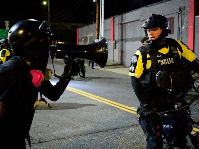 GettyImages-2239298178 A protestor shouts in a megaphone toward a Portland Police officer near an Immigration and