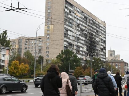 KYIV, UKRAINE - OCTOBER 10: People walk and cars drive past an apartment building damaged