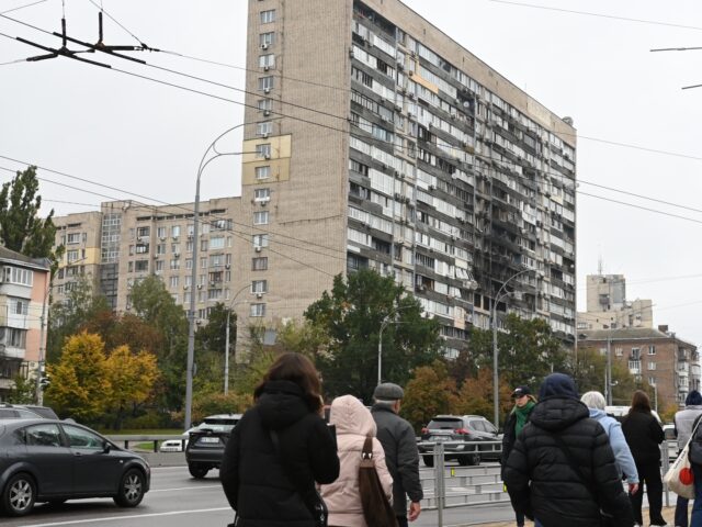 KYIV, UKRAINE - OCTOBER 10: People walk and cars drive past an apartment building damaged