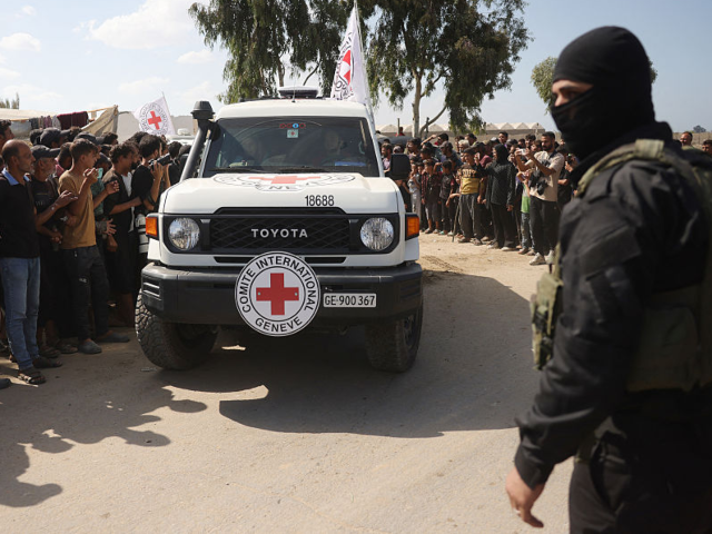 A Qassam Brigades militant stands guard as a crowd of Palestinians watches a vehicle of th