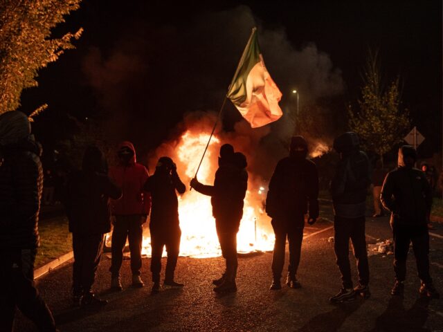 DUBLIN, IRELAND - OCTOBER 21: Protesters wave the Irish flag in front of bins set on fire