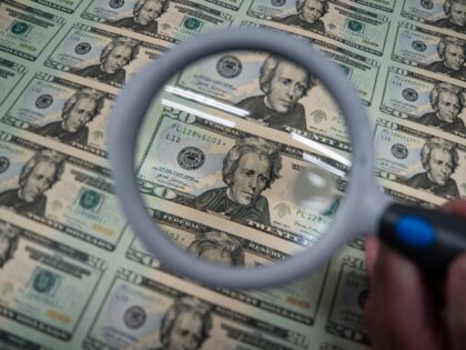 A worker holds a magnifying glass over a 50 subject $20 dollar note sheet after being prin