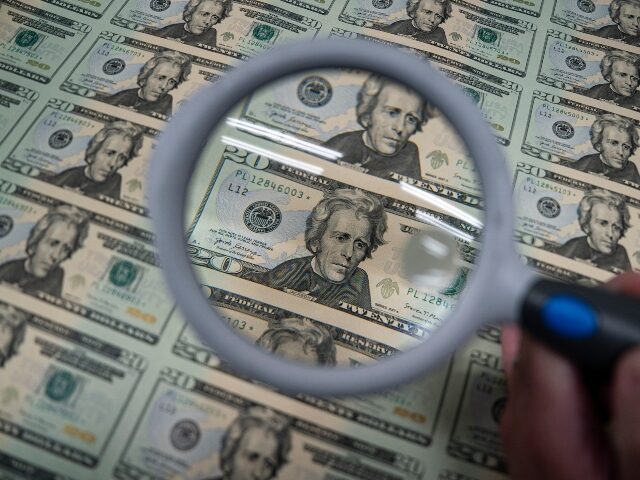 A worker holds a magnifying glass over a 50 subject $20 dollar note sheet after being prin