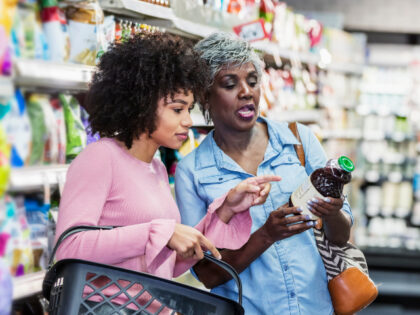 Two black women shopping together in a supermarket. The younger one, in her 20s, is carryi