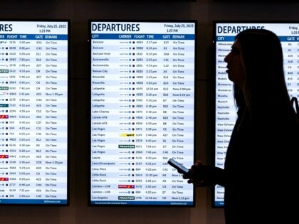 A woman walks past various screens displaying flight information at George Bush Interconti