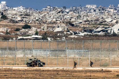 Israeli army soldiers walk towards an armoured vehicle at a position along the border fenc