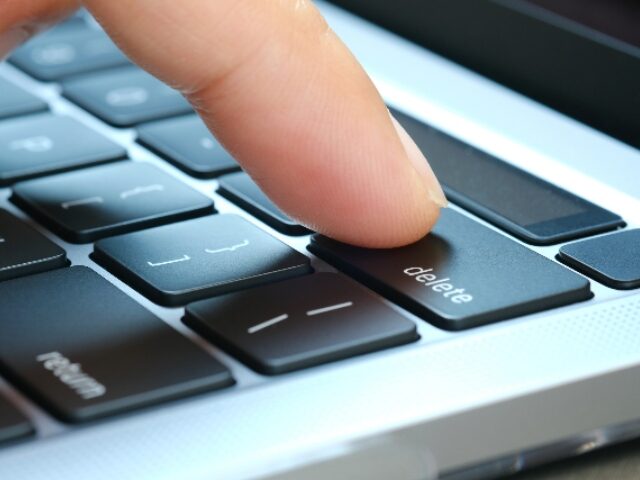 Finger of the computer user, he presses the delete button on the computer keyboard.