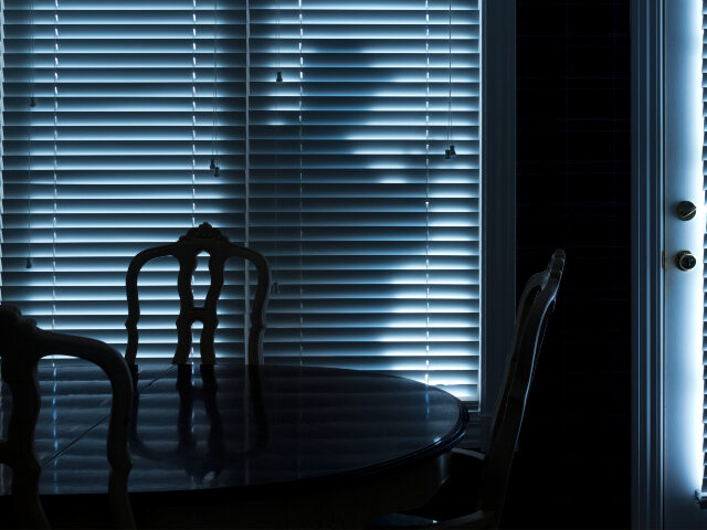 Silhouette of a burglar or thief sneaking up to back door at night. View from inside the r