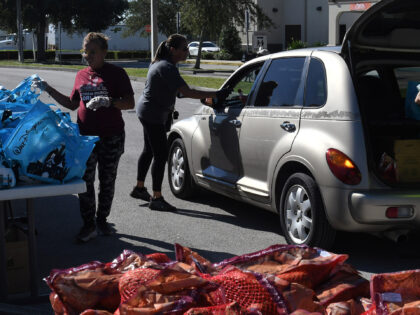 Volunteers place food items into a car at a disaster relief food distribution event sponso
