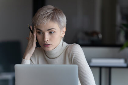Serious short hired business woman sit in front of laptop considering decision she looking