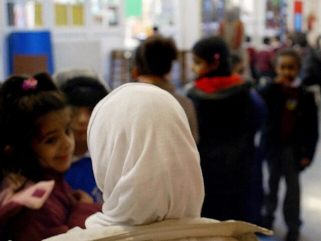 A young girl wearing a muslim headscarf stands in line talking with other girls before goi