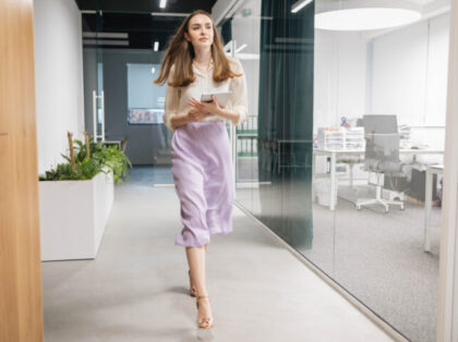 A young confident businesswoman walks down the hall of an office building holding a tablet