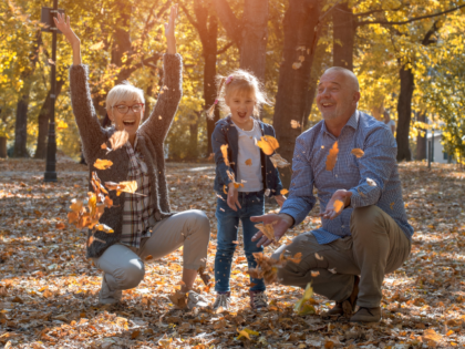 A little girl throwing leaves in the park with her grandparents in autumn