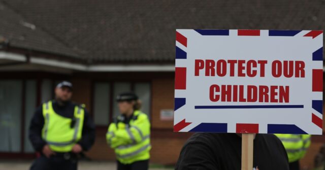 NORWICH, ENGLAND - AUGUST 17: A protester holds a sign saying 'Protect Our Children' in front of the police cordon outside the Brook Hotel during the rally on August 17, 2025 in Norwich, England. Protesters and counter-protesters have gathered outside hotels being used to house asylum seekers in recent weeks, as tensions flare over the government's policies on illegal migration, which has reached record numbers this summer. Some far-right politicians and campaigners have faced allegations of fanning the flames by spreading misleading data on crimes committed by foreign nationals, following isolated reports of migrant arrests over alleged crimes. (Photo by Martin Pope/Getty Images)
