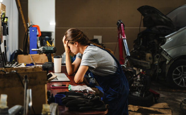 A worried woman entrepreneur in a car service shop, facing business difficulties. Bankrupt