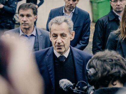 Former French President Nicolas Sarkozy leaves his home and walks past a crowd of people w