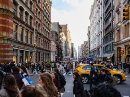 Many people are walking across the street in Manhattan New York City with a yellow taxi ca