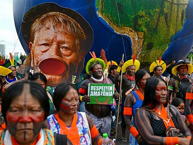 An Indigenous man holds a sign demanding respect for the Amazon next to an image of Indige