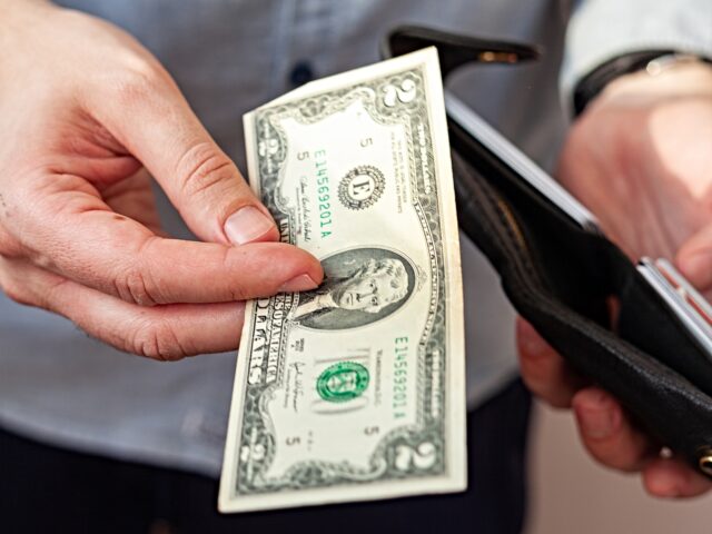 cash dollars A man in a denim shirt holds a wallet. Men's hands and take out or put a $ 2 bill in the w