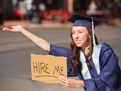 college graduate in gown holding hire me sign