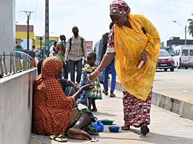 A pedestrian gives mony to a Nigerien woman sitting on the sidewalk with her children in A