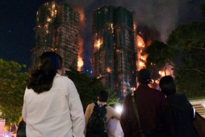 People look on as thick smoke and flames rise during a major fire at the Wang Fuk Court re