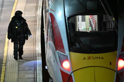 A Police officer walks on the platform alongside an LNER Azuma train at Huntingdon Station