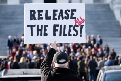 A protester holds a sign related to the release of the Jeffrey Epstein case files outside