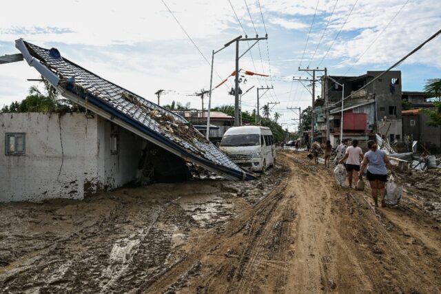 Residents walk along a mud-covered street in the aftermath of Typhoon Kalmaegi in Liloan,