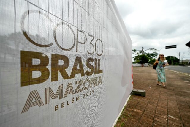 A woman walks past a banner with the COP30 UN Climate Change Conference logo outside the H